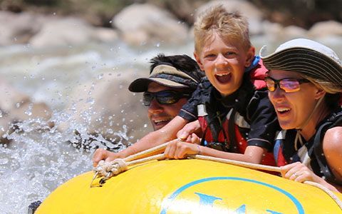 A smiling family rides through whitewater on a yellow raft