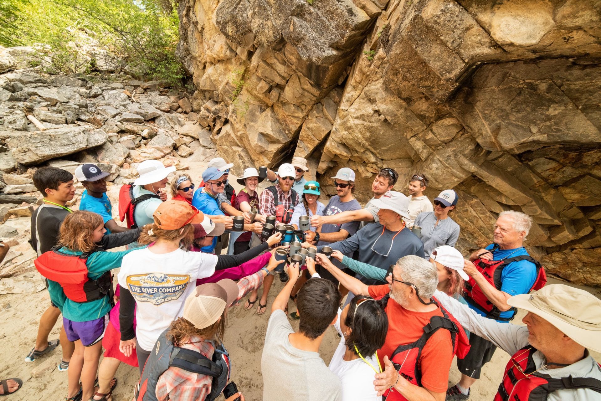 A rafting group shares a toast beside a rocky canyon wall