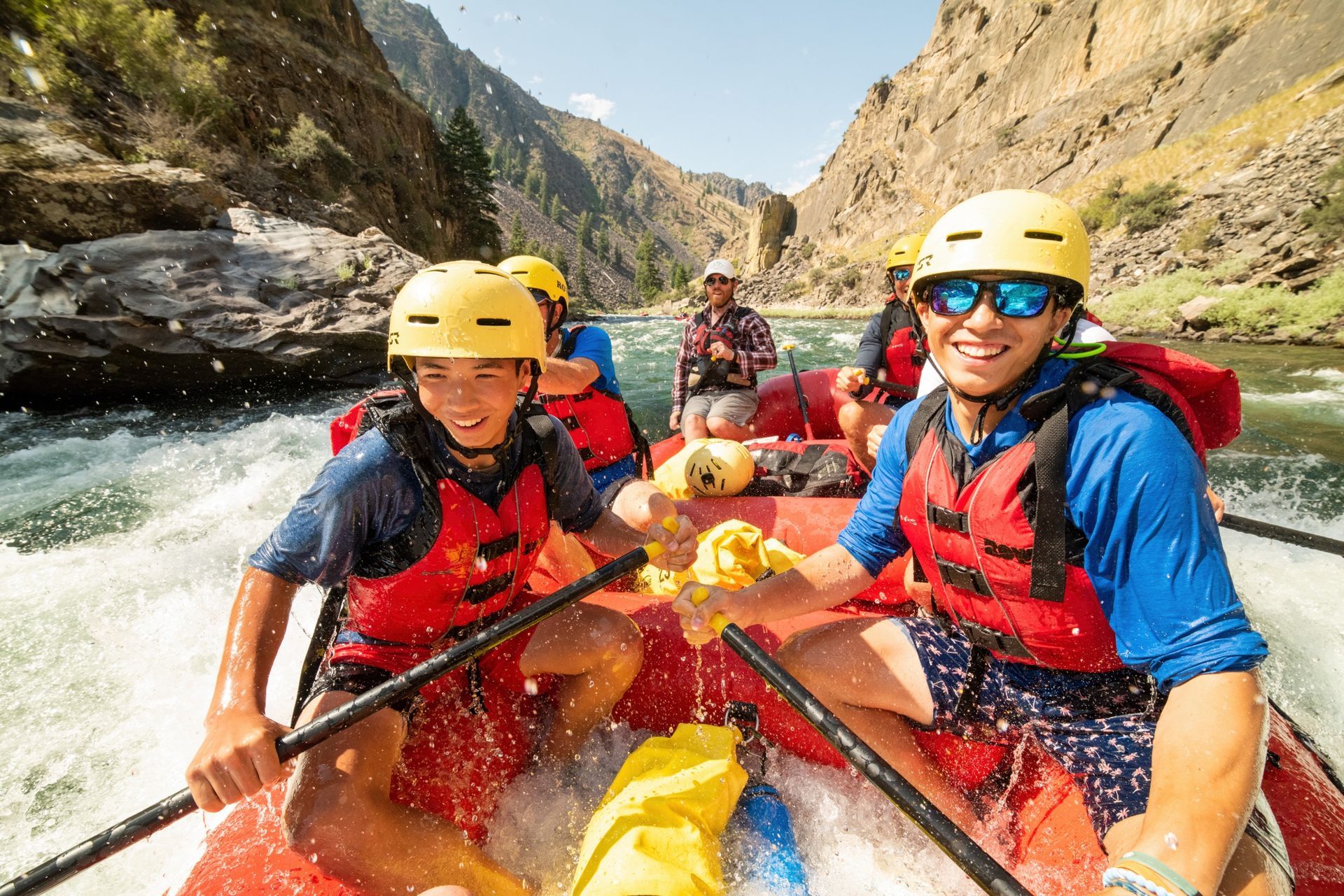 Smiling paddlers in helmets and life jackets aboard a red raft