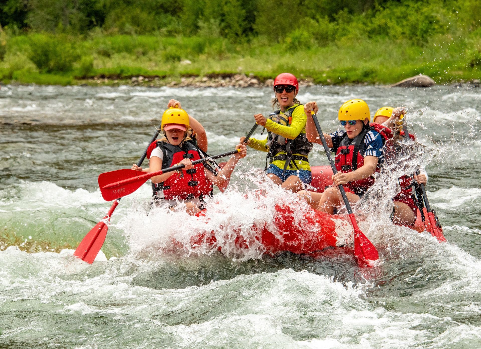A group of smiling guests on a paddle boat splashes through a rapid on an Idaho river