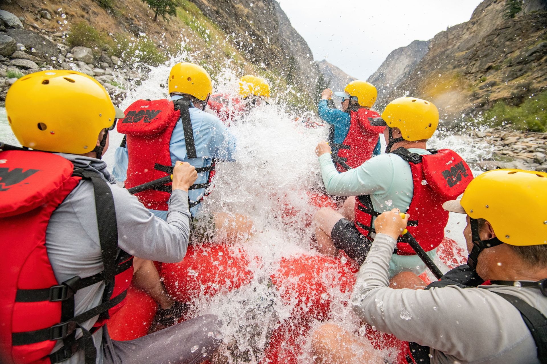 Water splashes over paddlers wearing helmets inside a raft
