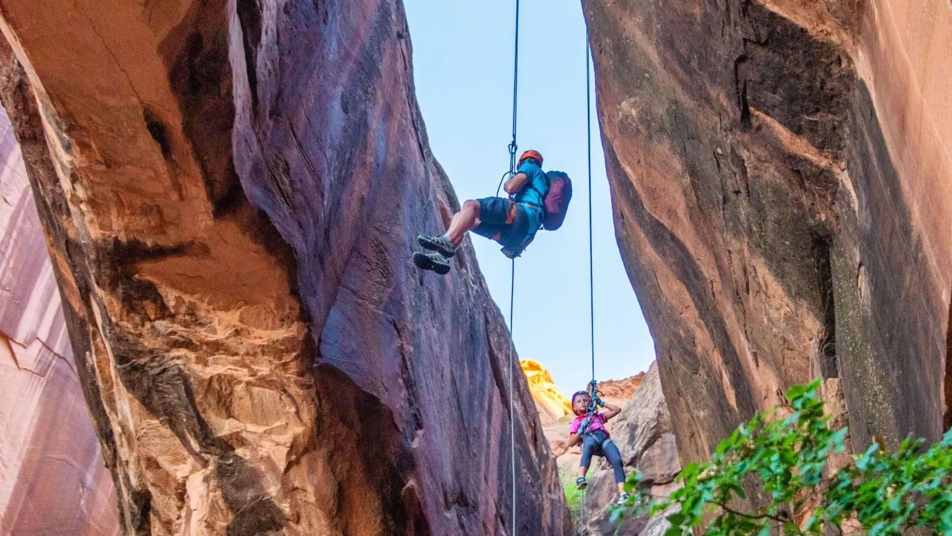 Two people rappel between sandstone canyon walls near Moab
