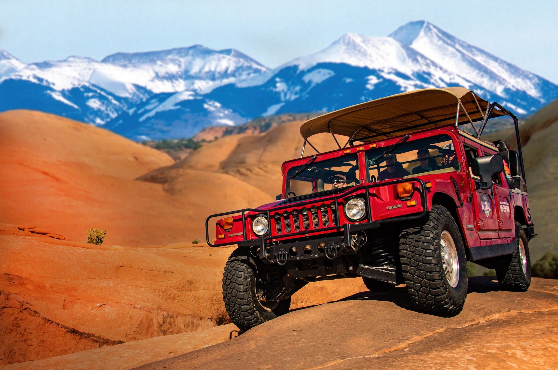 A red Hummer on sandstone with the La Sal Mountains behind it
