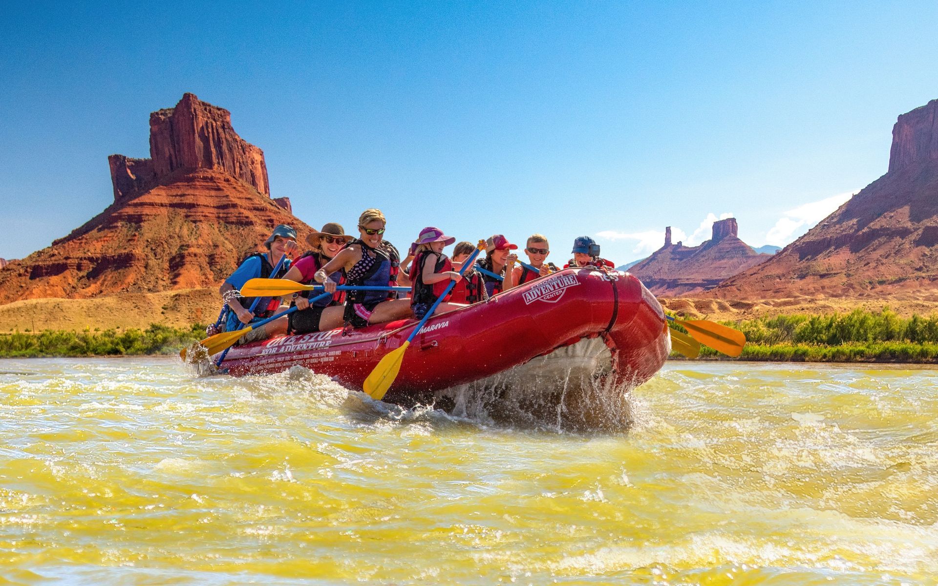 A red paddle raft runs a rapid below Castle Valley’s cliffs