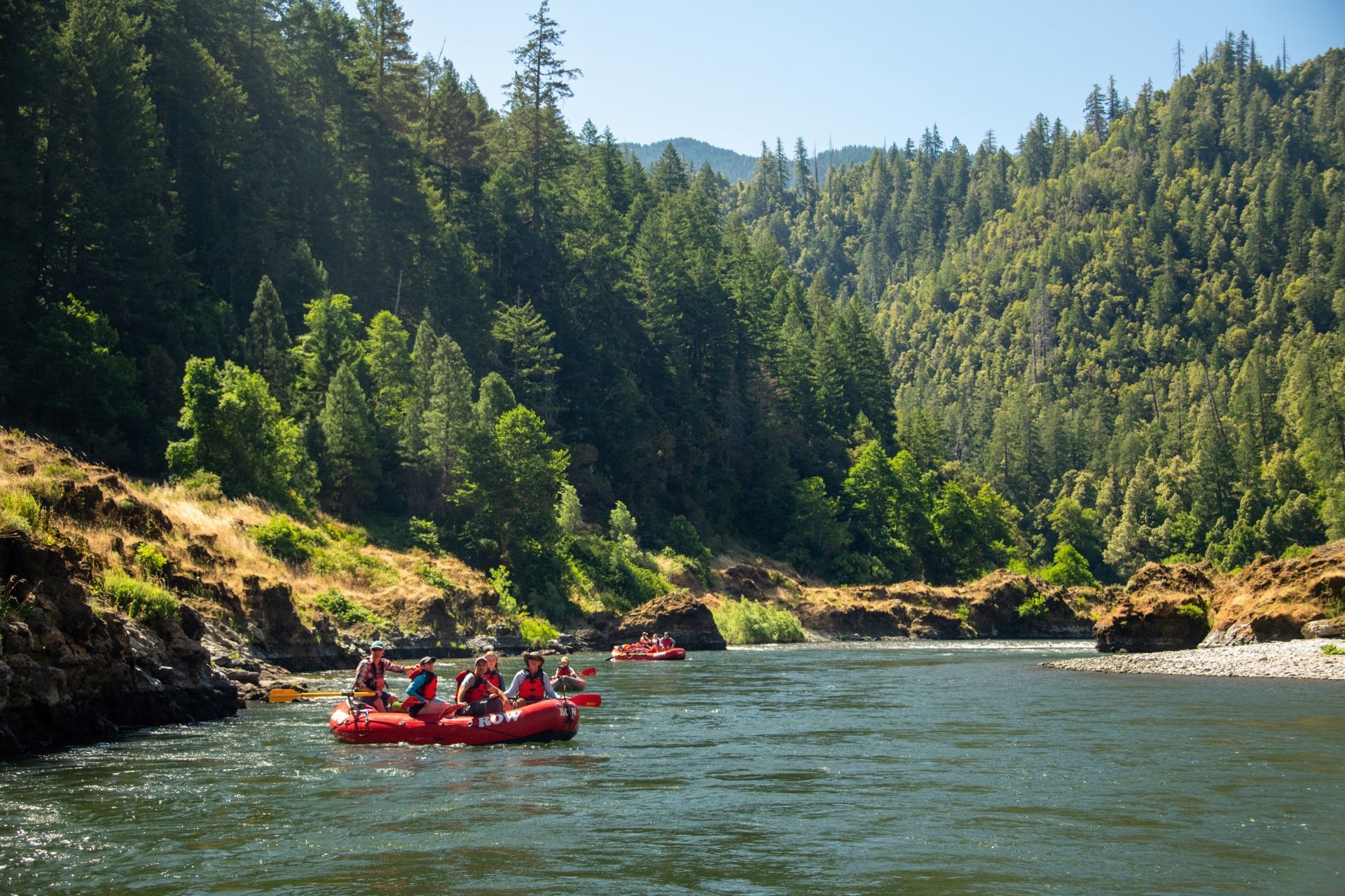 Red paddle boat floats on green river water surrounded by densely forested hills.