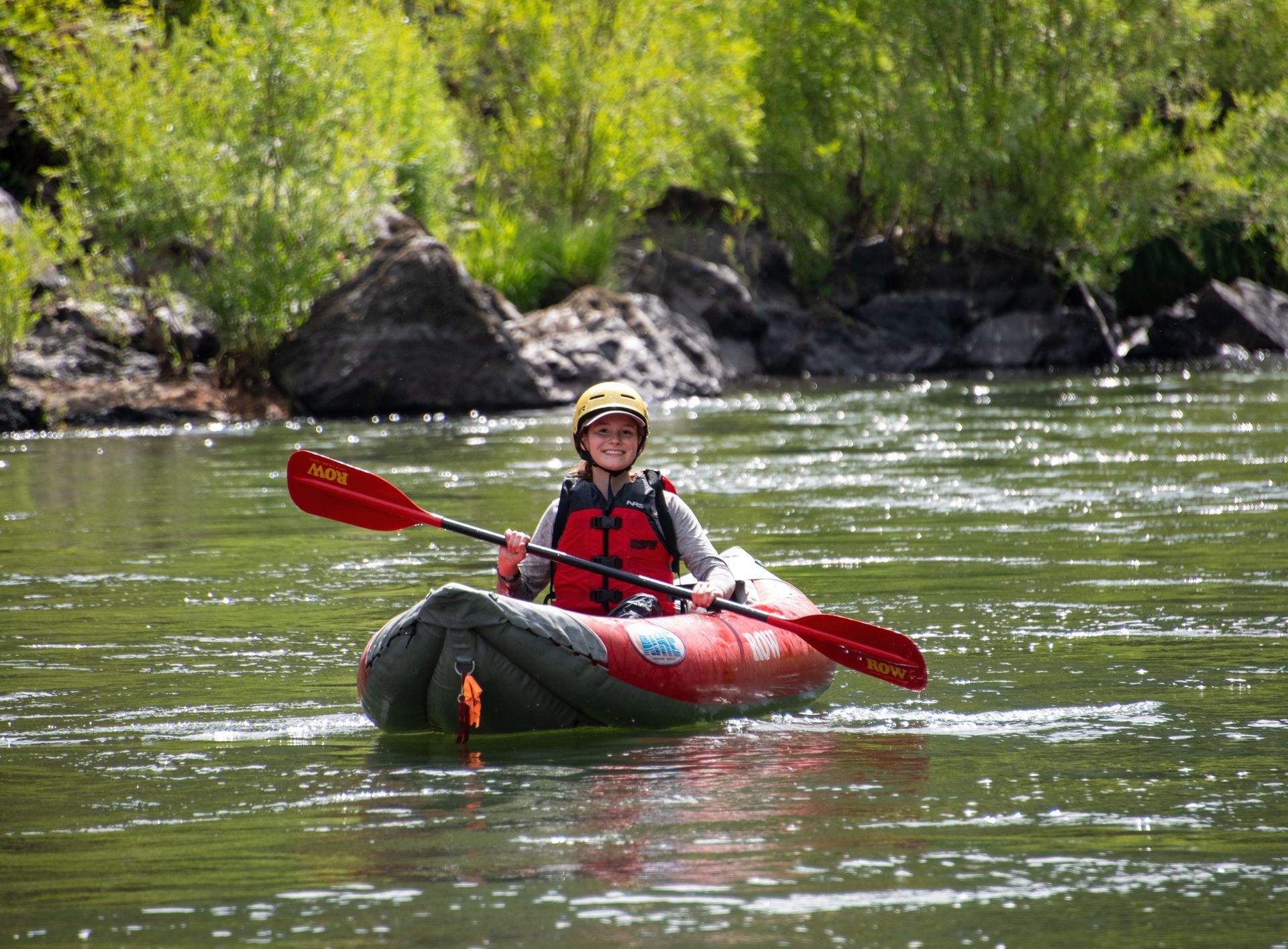 Paddler in a red inflatable kayak on calm river water