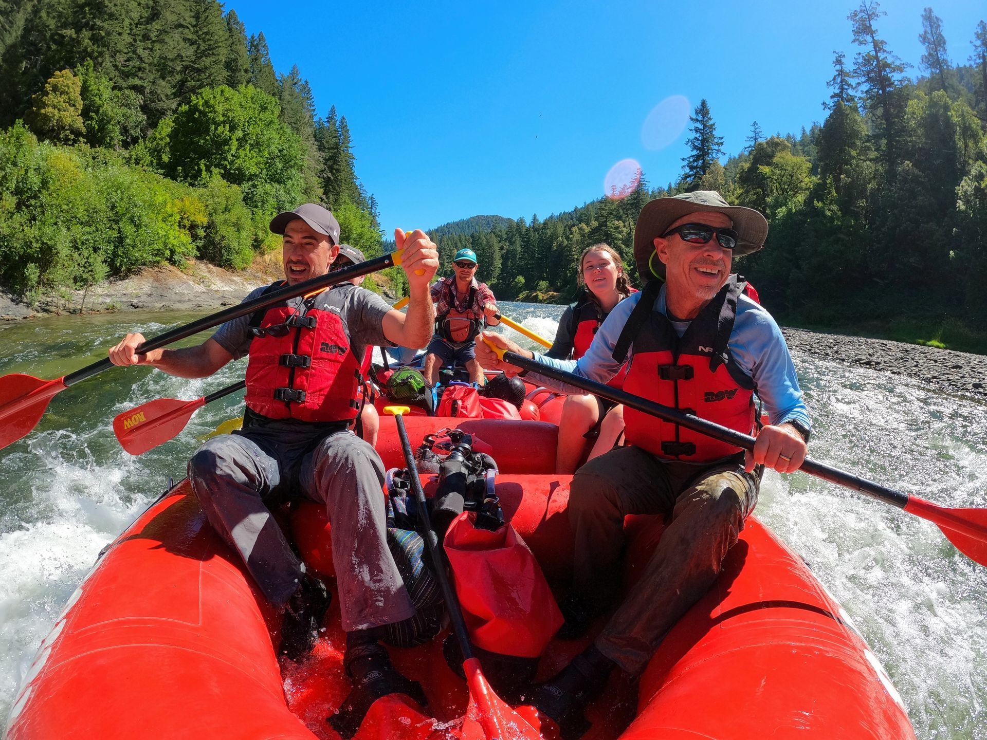 Smiling paddlers ride a red raft on the Rogue River