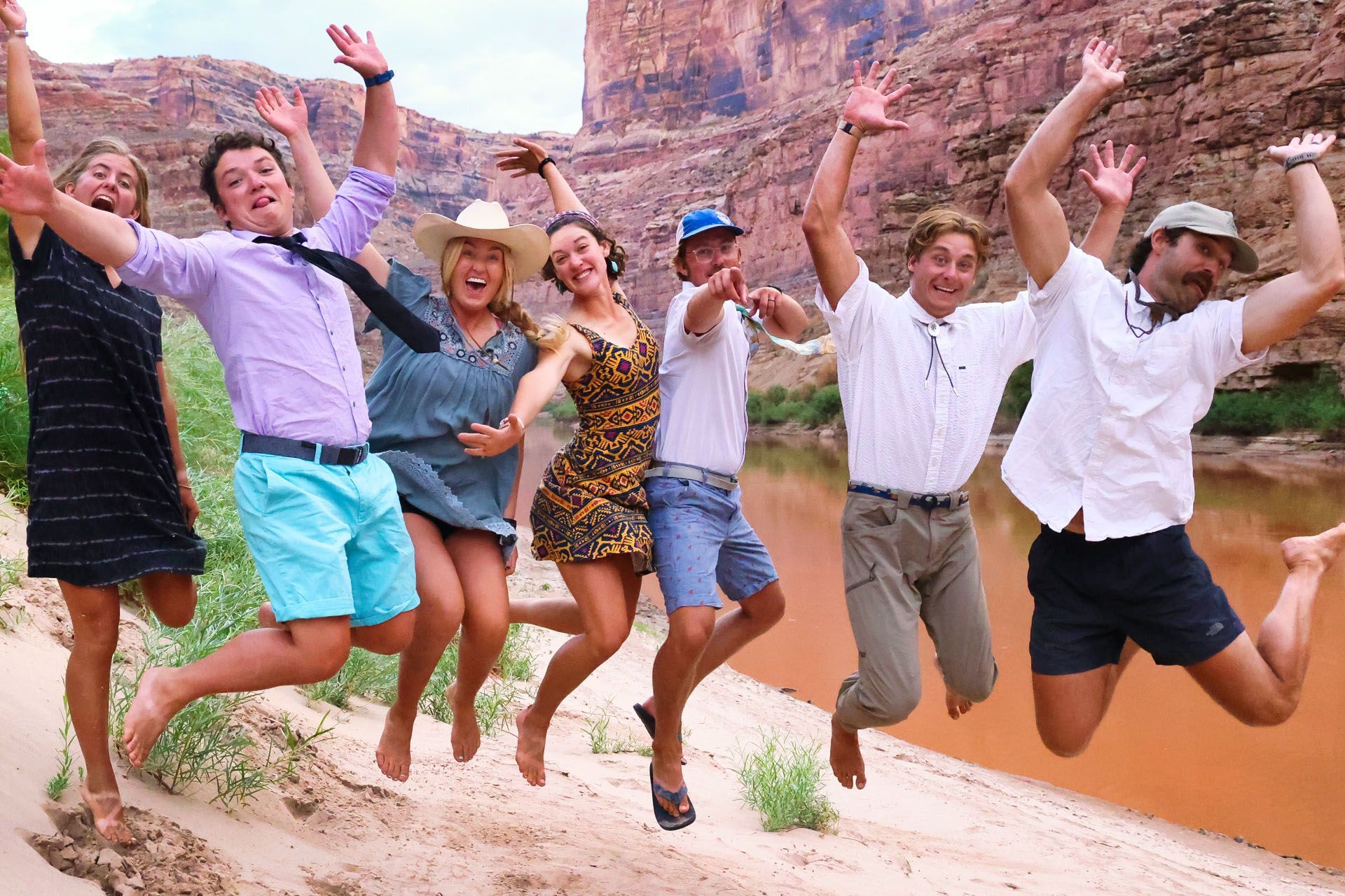 A group jumps together on a sandy canyon beach
