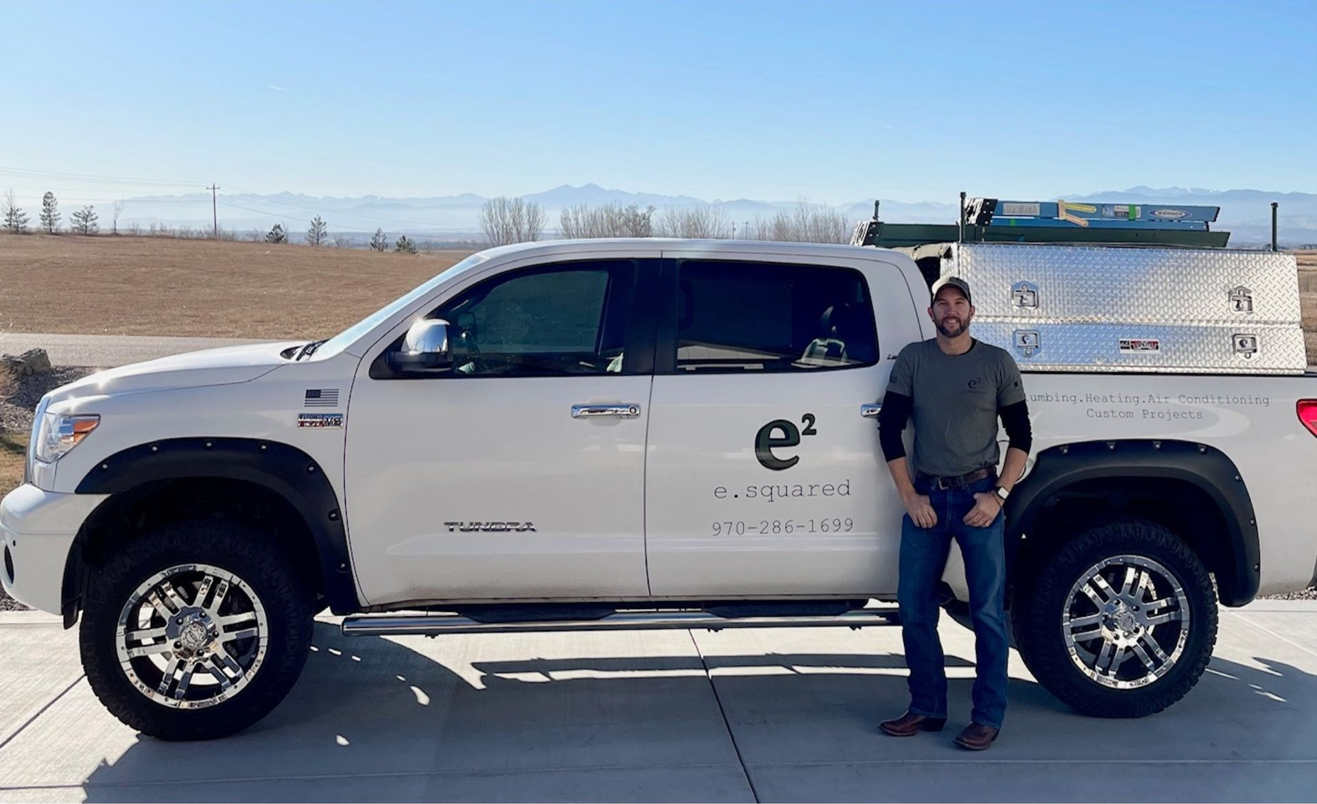 Man stands beside white Toyota Tundra truck in front of a house on a sunny day.