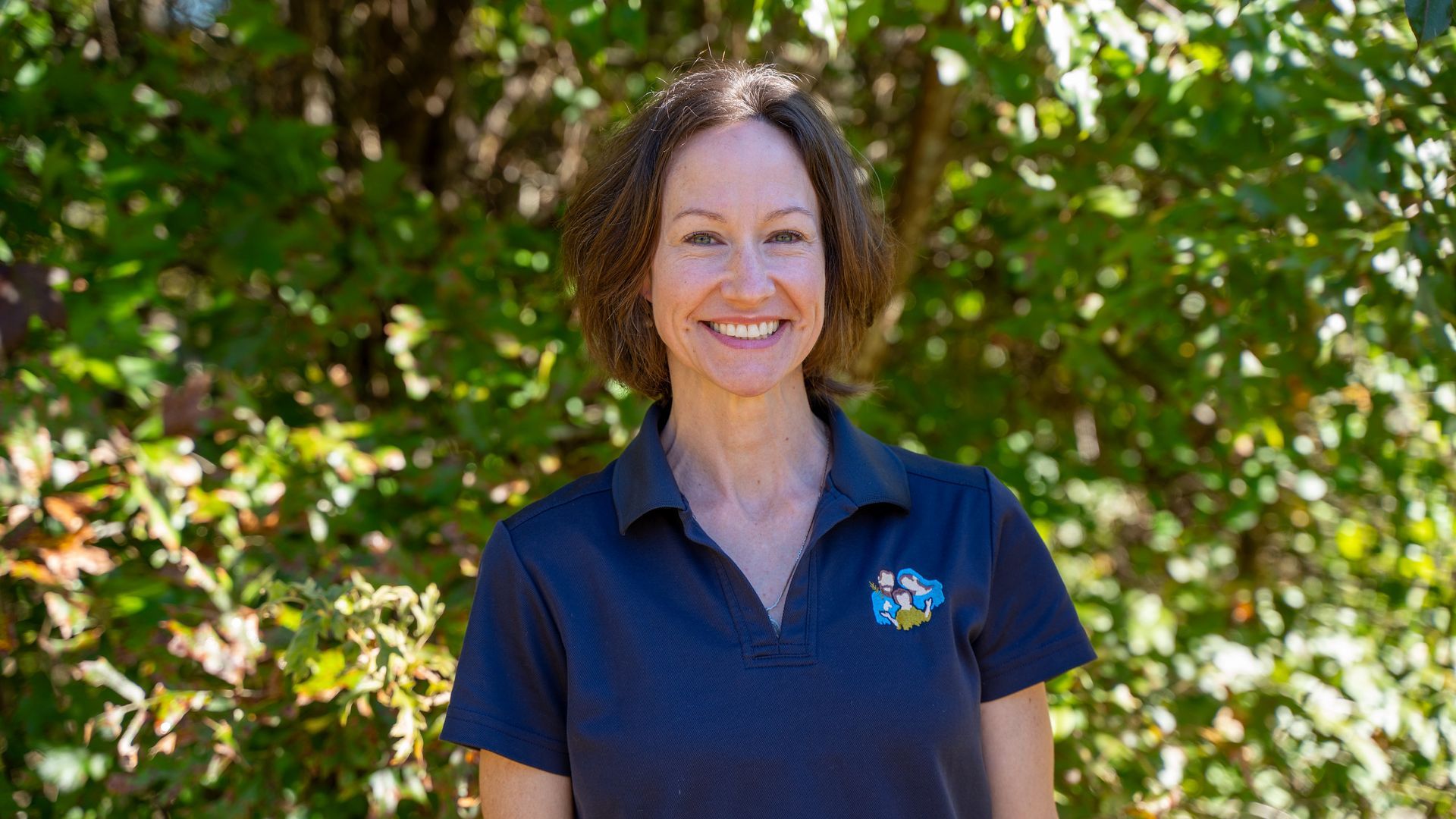 A woman wearing a floral shirt and necklace smiles for the camera