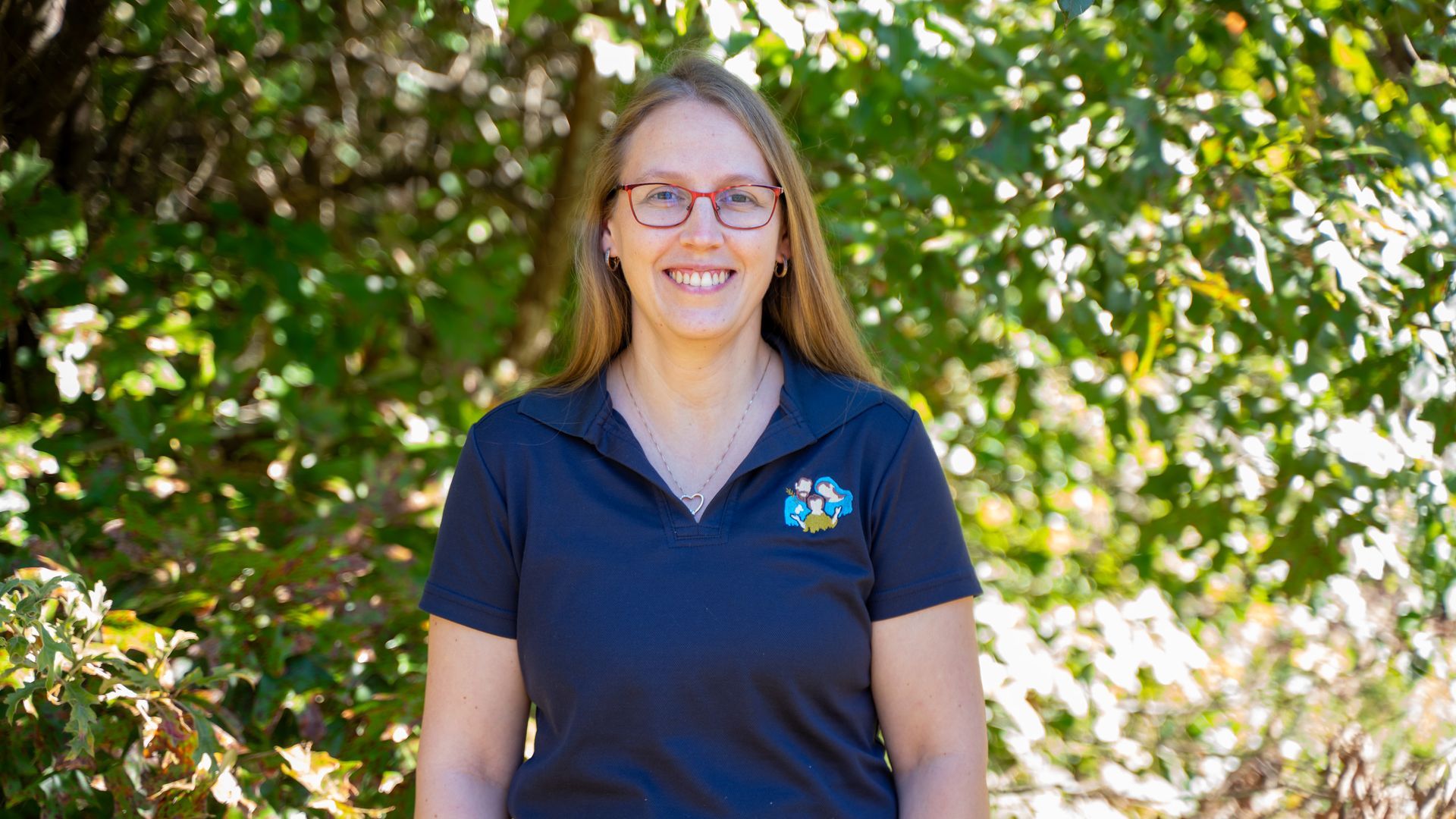 A woman in a purple shirt is smiling in front of a tree.