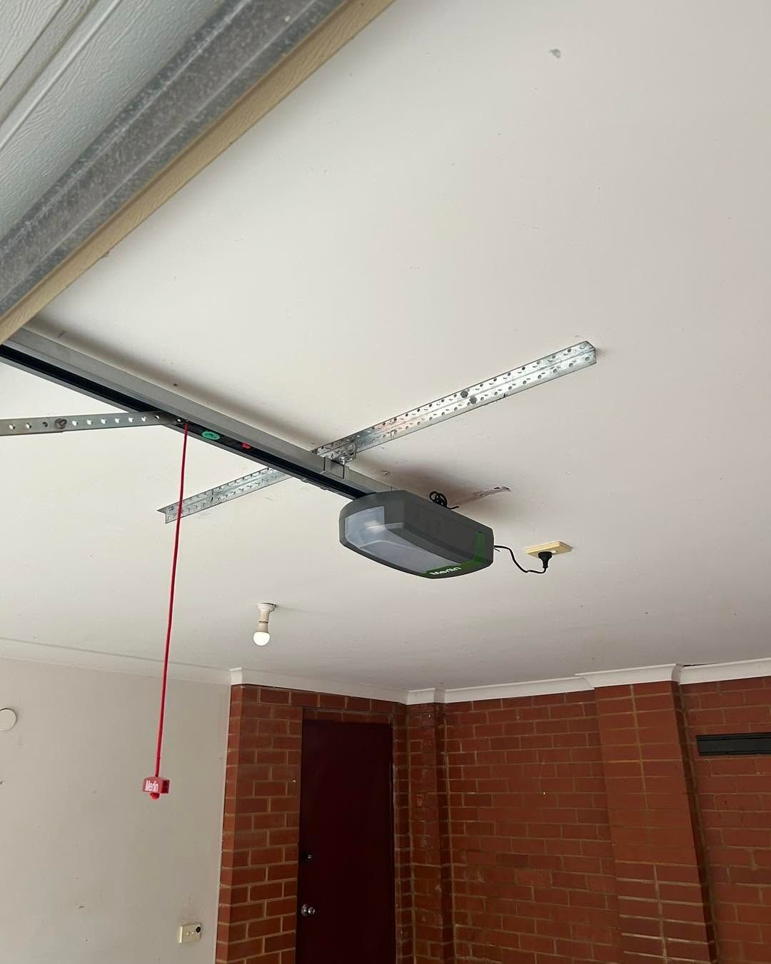 Garage ceiling with opener rail, red pull cord, and brick walls.