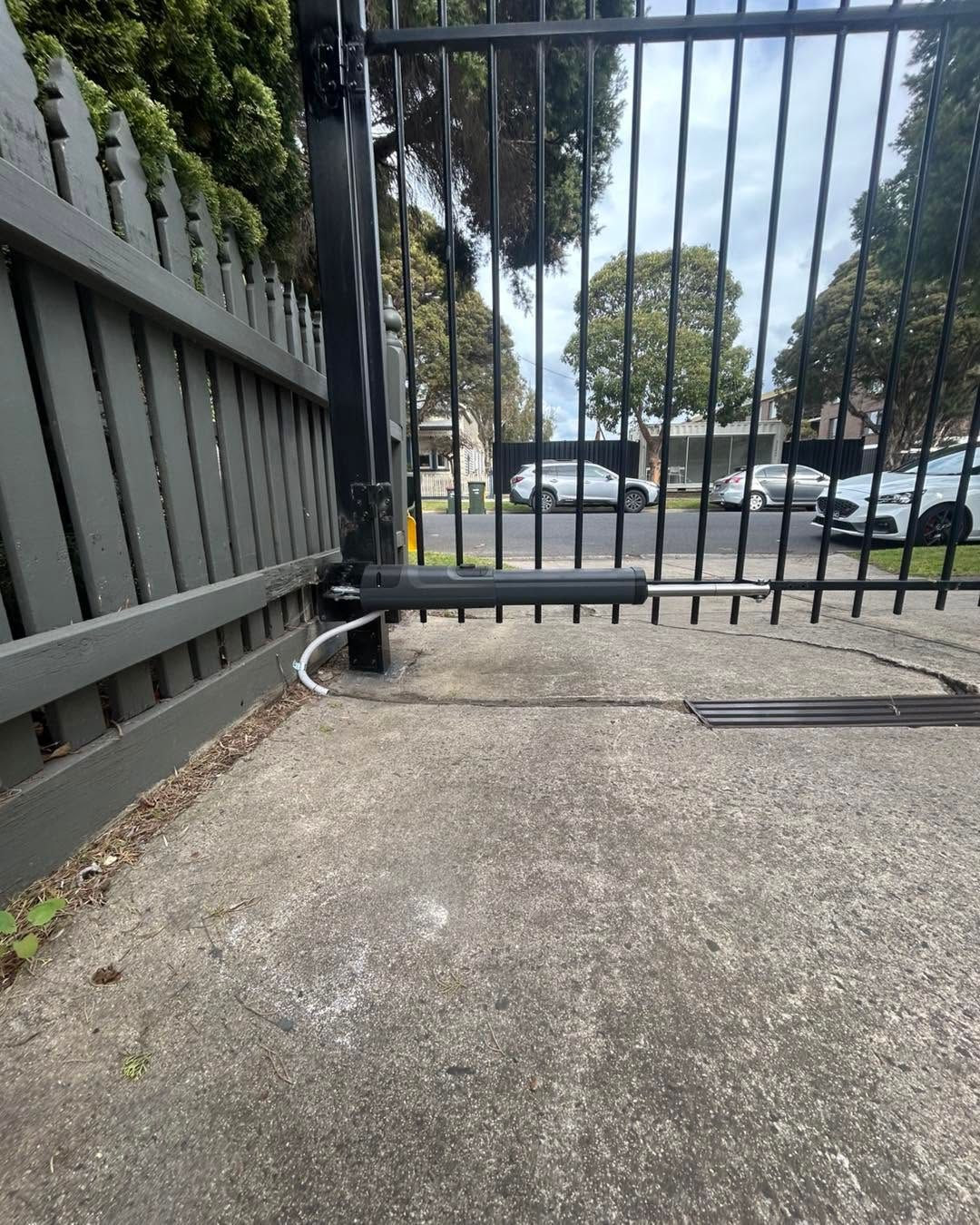 Concrete walkway blocked by a metal gate and low barrier, with parked cars visible beyond.