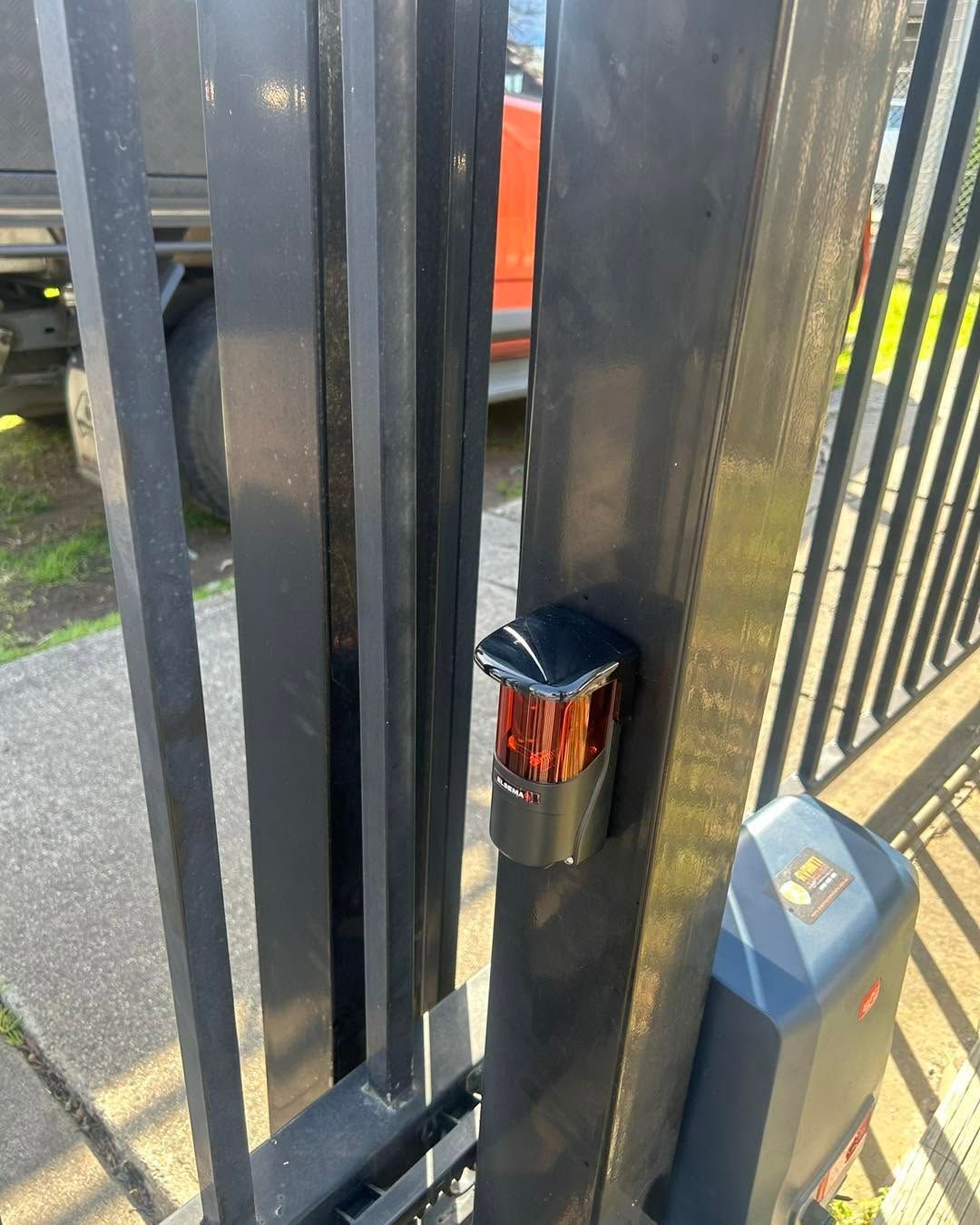 Close-up of a black metal gate latch with a small cylindrical lock and gray post beside it.