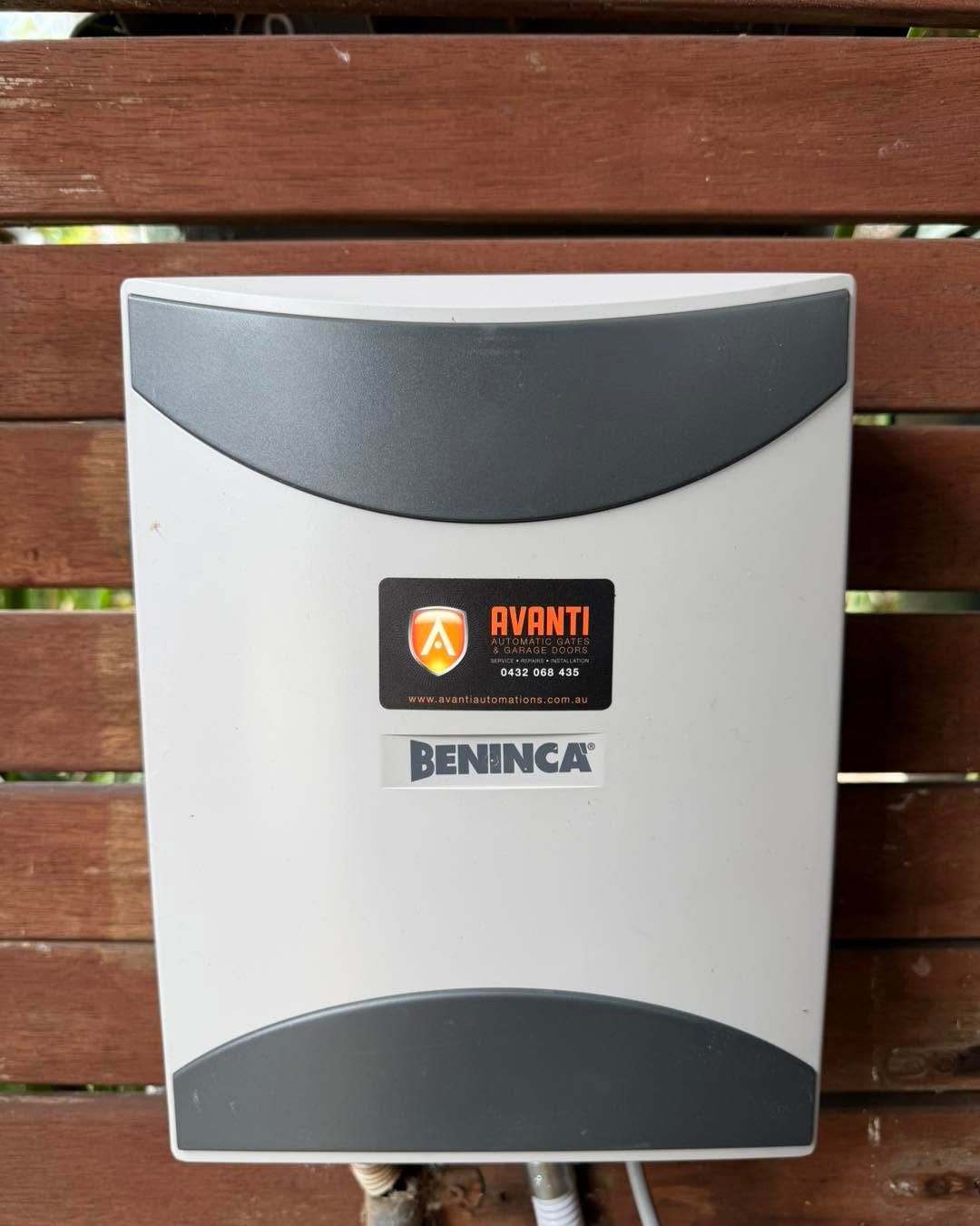 White and gray Beninca wall-mounted gate opener unit with logo on a wooden slat background