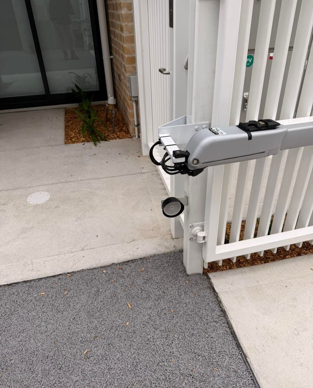 Folded mobility scooter parked beside a white fence on a gray walkway near a building entrance