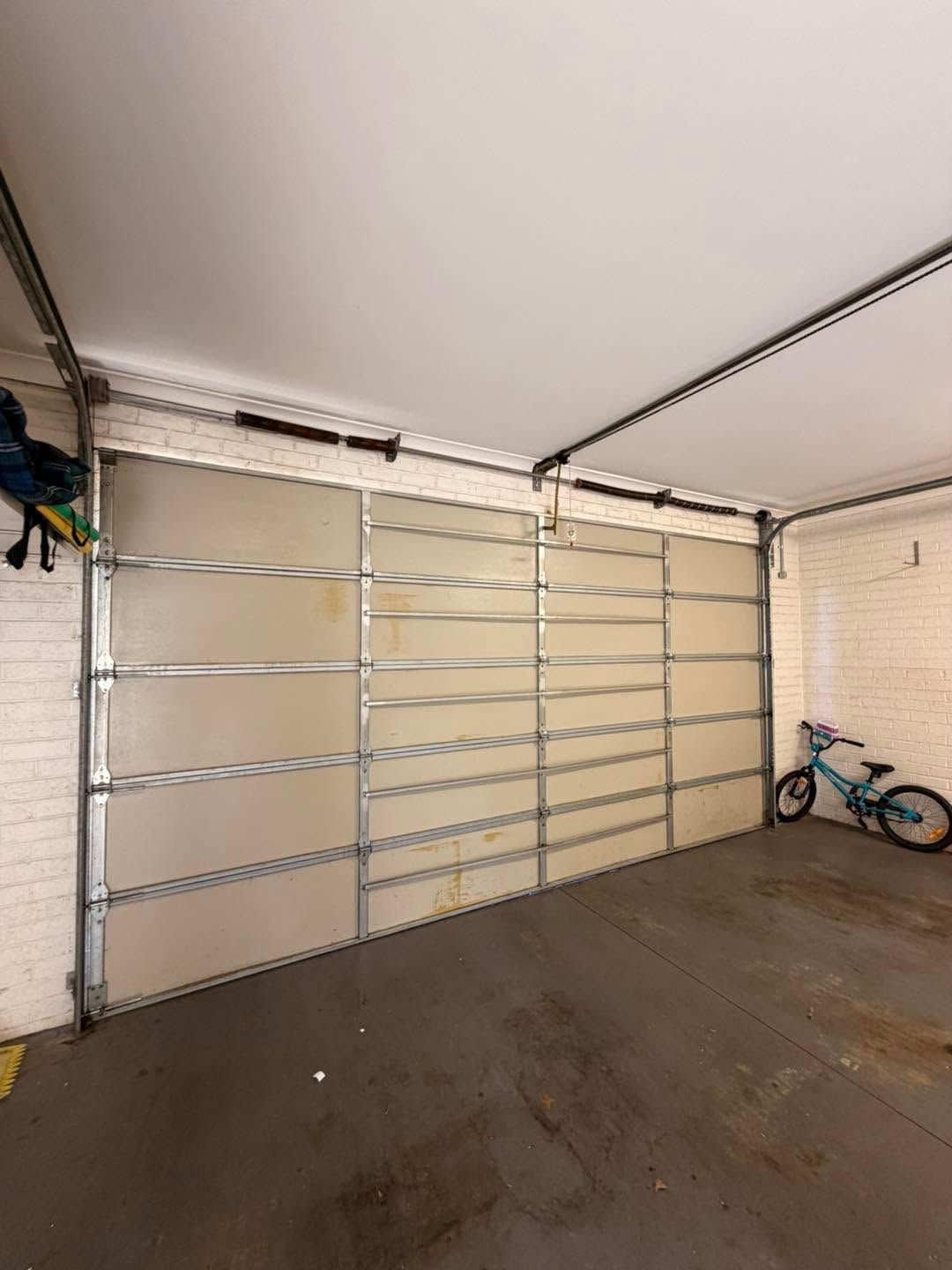 Garage interior with a white sectional door and a blue bicycle parked against the wall.