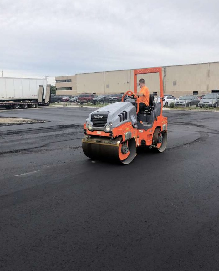 A man is driving a roller on a parking lot