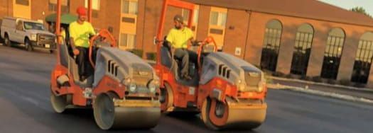 Two rollers are driving down a street in front of a building. Two rollers are driving down a street in front of a building.