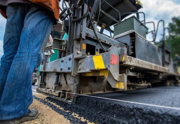 A man is standing next to a machine that is laying asphalt on a road.
