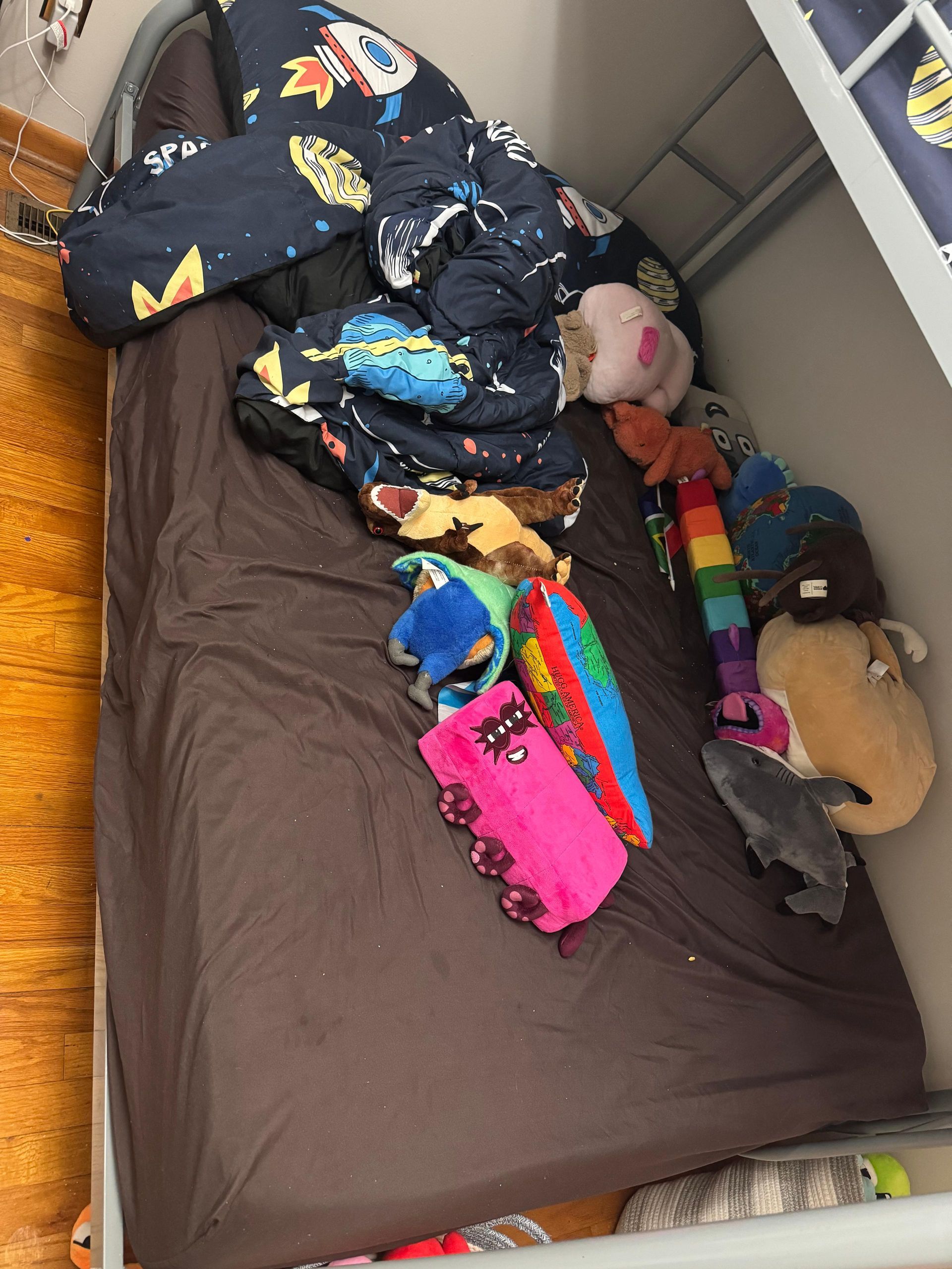 Messy bed with dark bedding and several stuffed animals and colorful toys scattered on top.