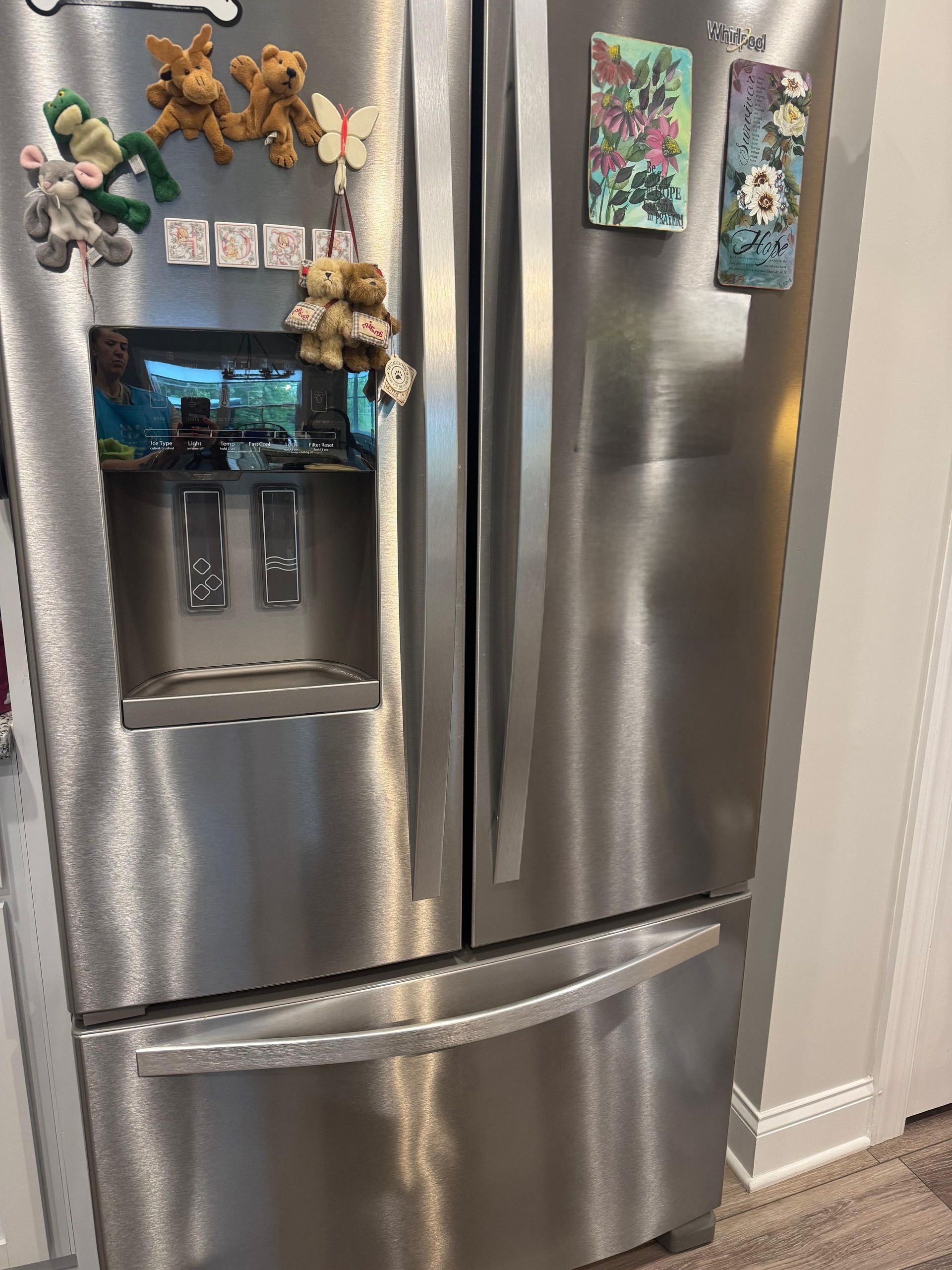 Stainless steel fridge with magnets, photos, and a water dispenser in a kitchen. Stainless steel fridge with magnets, photos, and a water dispenser in a kitchen.