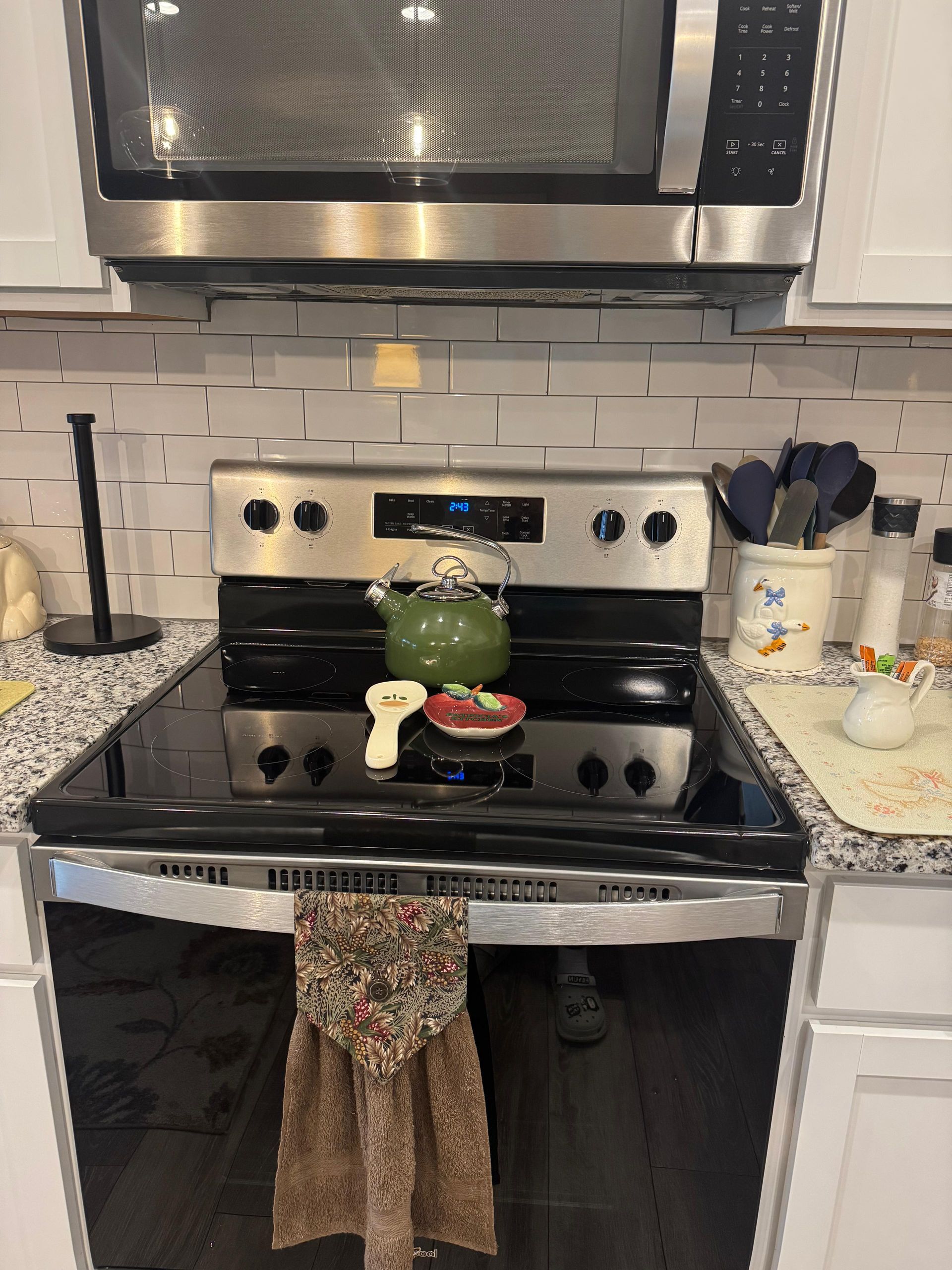 Kitchen stove with a green frog decoration, towel on the oven door, and utensils on the countertop. Kitchen stove with a green frog decoration, towel on the oven door, and utensils on the countertop.