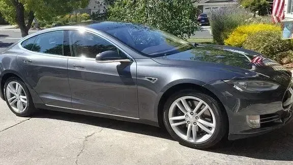 Gray sedan parked in a driveway, front side view with trees and a house in the background