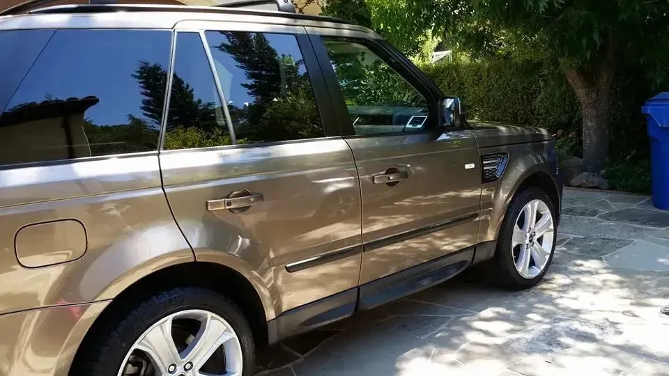 Tan SUV parked in a sunny driveway beside palm trees and a blue trash bin