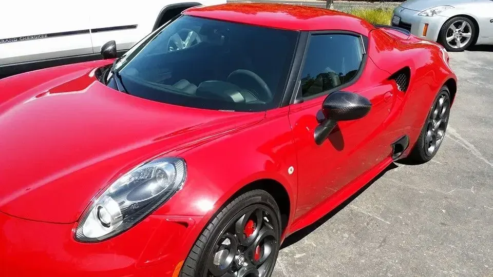 Red sports car parked outdoors in sunlight, viewed from the front-left side.