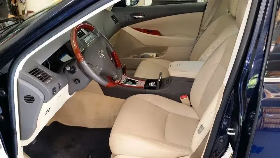 Beige car interior with open driver’s door, steering wheel, center console, and front seats visible