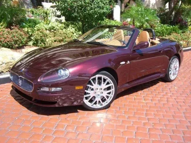 Maroon convertible sports car parked on a brick driveway beside greenery