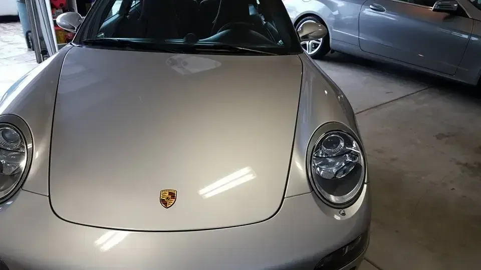 Front view of a silver Porsche 911 parked in a garage, with another car beside it