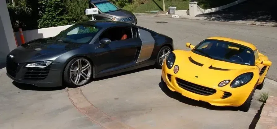 Black Audi R8 and yellow sports car parked on a sunny driveway, front view