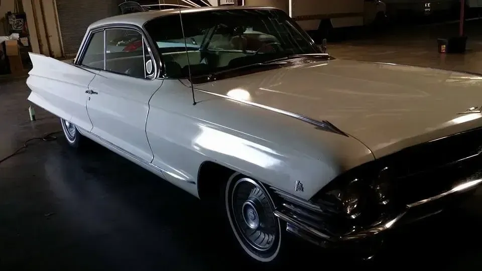 White vintage car parked indoors under dim lighting, front-left view