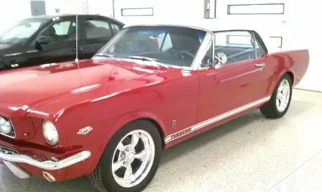 Red classic convertible sports car with white top, parked indoors in a bright garage