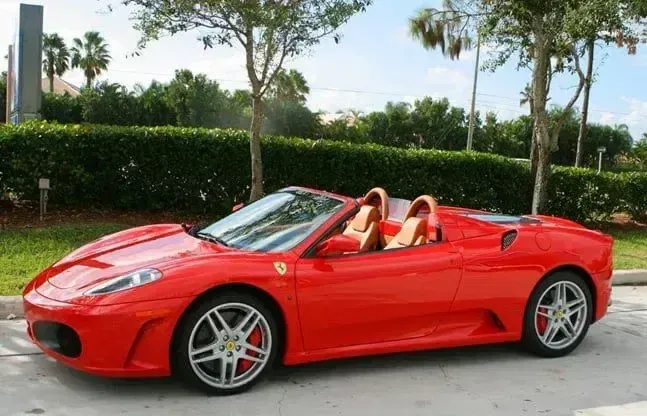 Red convertible sports car parked on a street beside hedges and trees