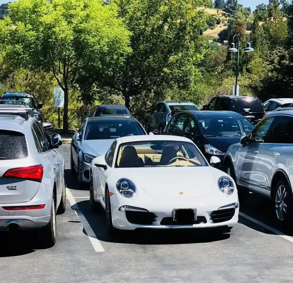 White convertible sports car parked in a crowded lot among other vehicles and trees