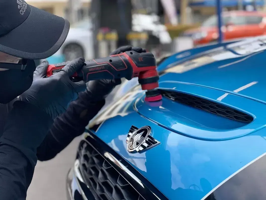 Worker polishing a blue car hood with a power buffer in an auto shop