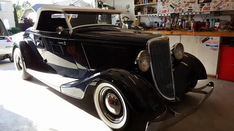 Black vintage classic car in a garage, with whitewall tires and chrome details.