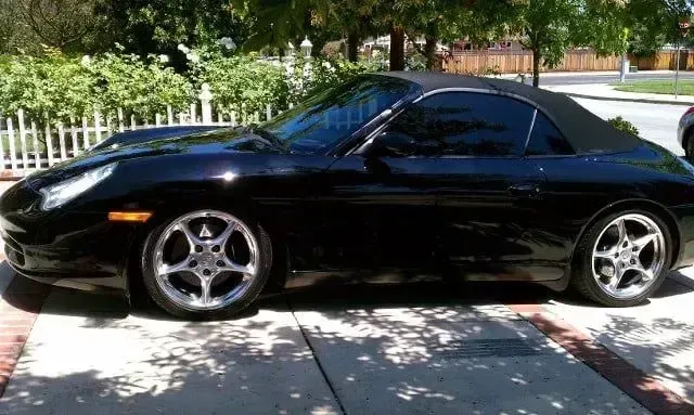 Black sports coupe parked in a sunny driveway, side view with tinted windows and silver rims