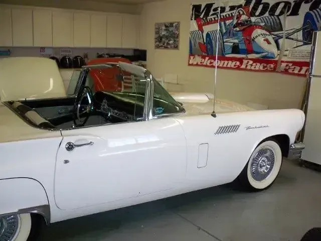 White classic convertible in a garage, hood open, with a Marlboro racing banner on the wall