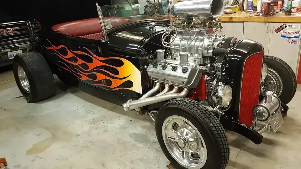 Custom hot rod with orange flames parked in a garage, front-left view