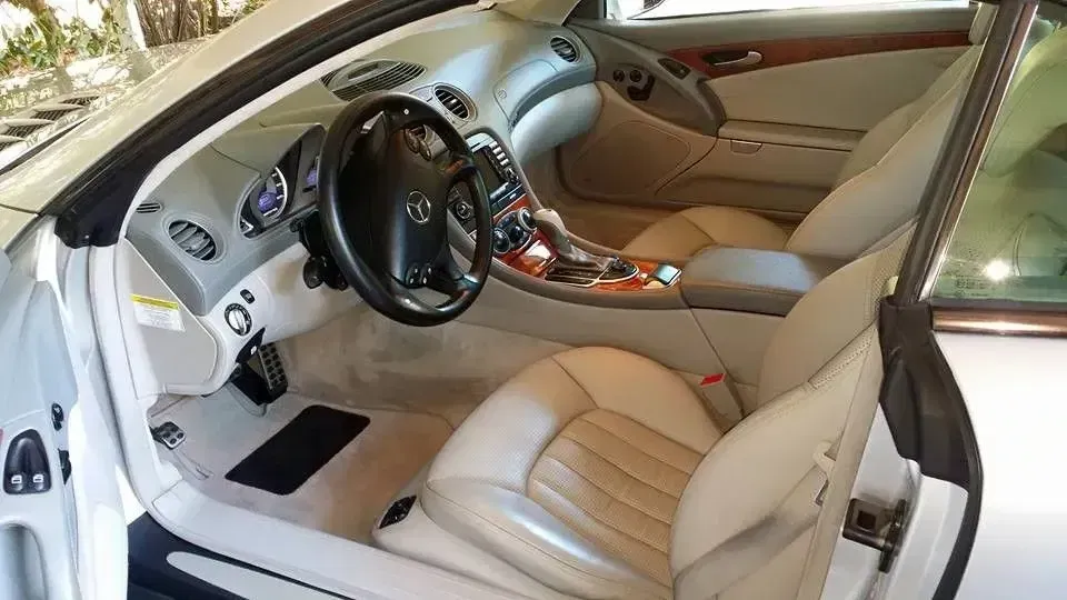 White luxury car interior with beige leather seats, black steering wheel, and open driver’s door