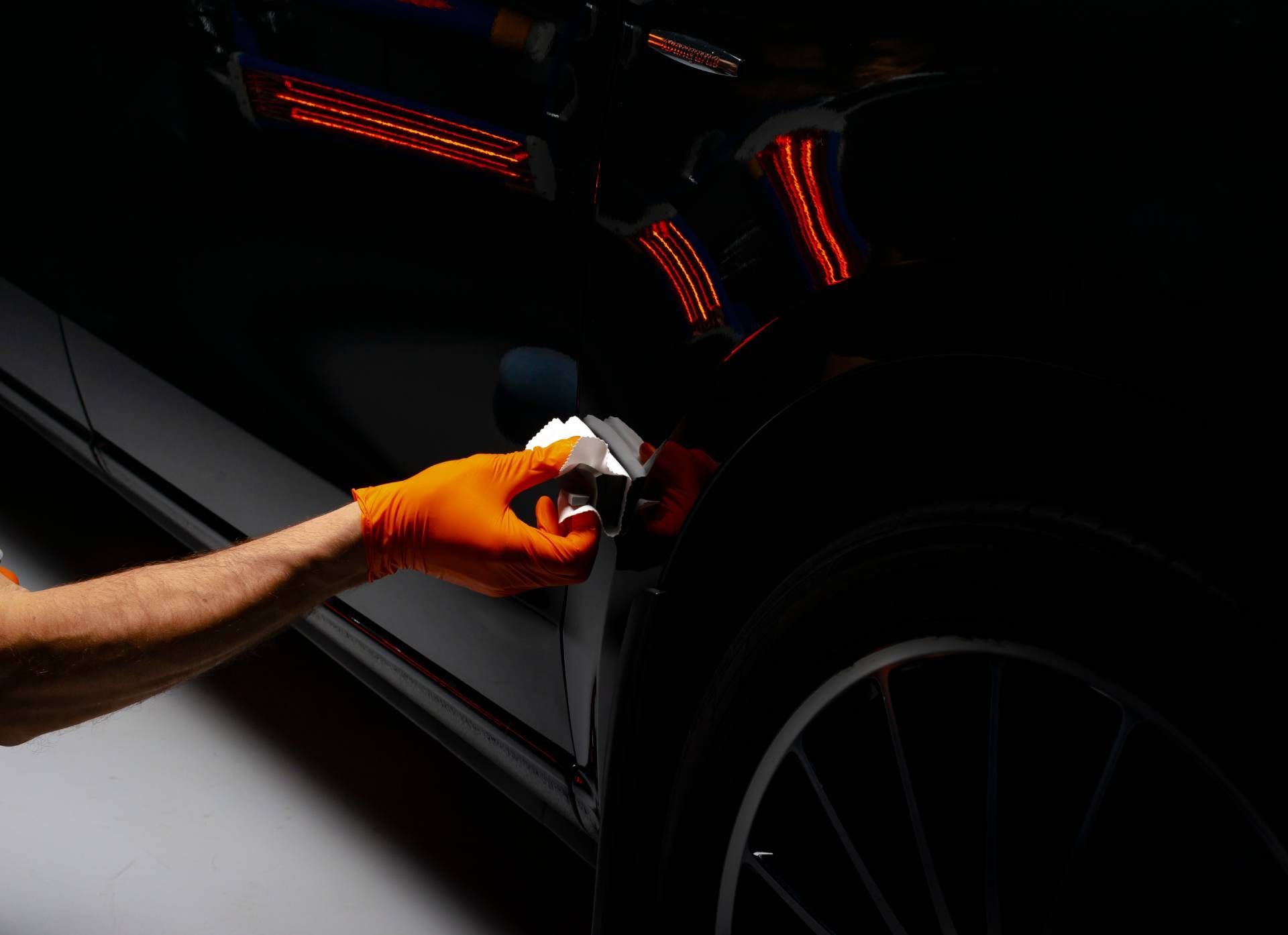 Gloved hand cleaning a black car’s body panel with a cloth at night