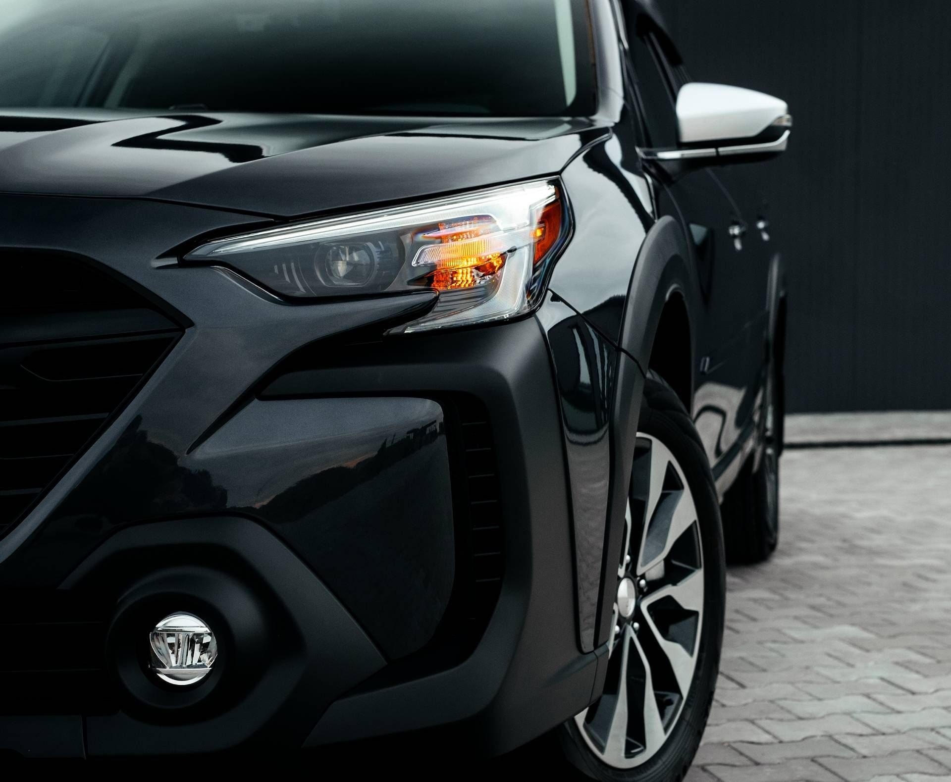 Black car front close-up with illuminated headlight and fog light, parked on a paved surface