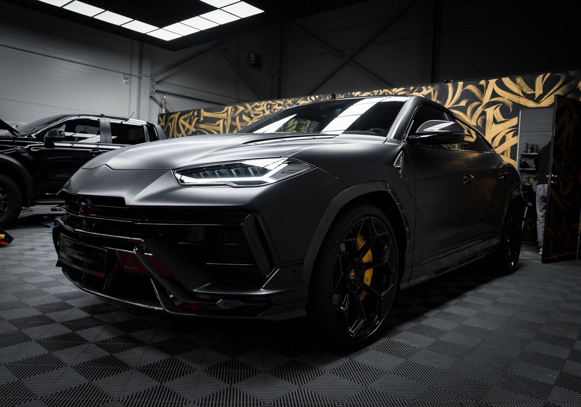 Black sports SUV in a dim garage, front view with matte finish and yellow brake calipers