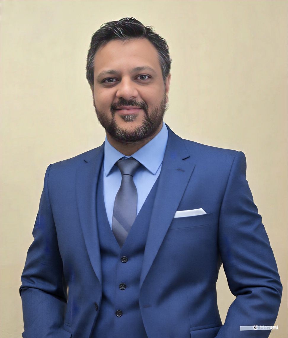 Smiling person in a blue suit and tie against a plain beige background