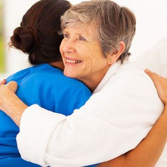 Two people hugging, one in blue and one in white, smiling warmly indoors