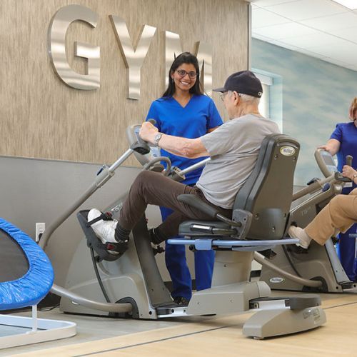Physical therapy gym with a therapist assisting a seated patient on exercise equipment